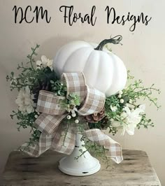 a white pumpkin decorated with flowers and greenery on top of a wooden table next to a sign that says, mom floral designs