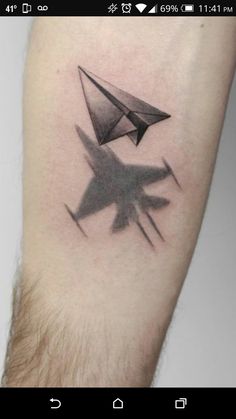 a black and white photo of a paper airplane tattoo on the left arm, with an origami plane in the middle