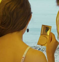 a woman holding up a small box with a butterfly in it's mouth next to the ocean