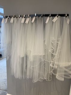 white tulle curtains hanging on the wall with price tags attached to them and hang from hooks