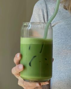 a woman holding a green drink with a straw in it