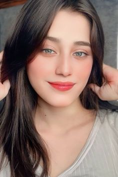 a woman with long brown hair and blue eyes is posing for the camera while wearing a gray shirt