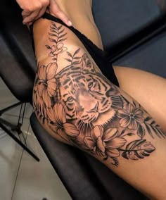 a woman's thigh with a tiger and flowers tattoo on her leg, sitting in a chair