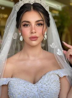 a woman in a wedding dress wearing a tiara and holding her finger up to the camera