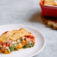 a white plate topped with lasagna covered in cheese and sauce next to a red casserole dish