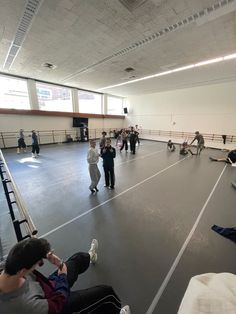 many people are sitting on the floor in an empty gym with one person taking a photo