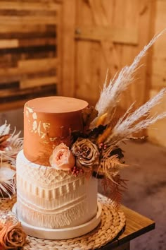 a three tiered wedding cake with flowers and feathers on the top is sitting on a table