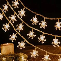 snowflake lights are hanging from a string on a wooden table next to a lit candle