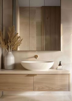 a white bowl sink sitting on top of a wooden cabinet next to a vase with flowers