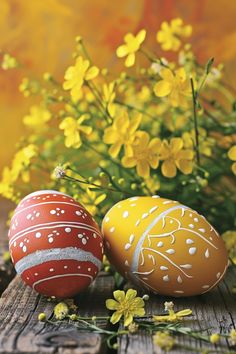 two painted easter eggs sitting on a wooden table next to yellow flowers and wildflowers