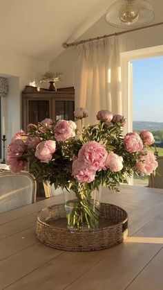 a vase filled with pink flowers sitting on top of a wooden table next to a window