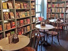 a library filled with lots of books next to a table and chairs in front of a window