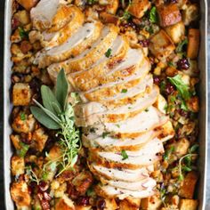 sliced chicken and stuffing in a pan with fresh herbs on the side for garnish