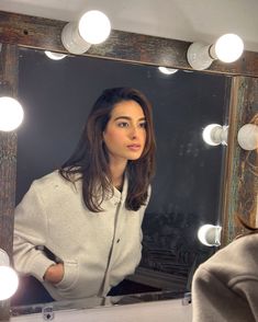 a woman standing in front of a mirror looking at her reflection with lights around her