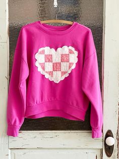 a pink sweater hanging on a door with a checkered heart painted on it's chest