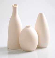 three white vases sitting next to each other on top of a table in front of a white background