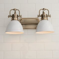 two lights are on the wall in front of a white brick wall and floor tile