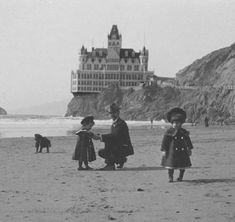 an old black and white photo of people on the beach with a castle in the background