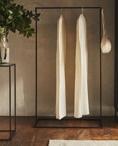 two white dresses hanging on clothes racks next to a potted plant in a room