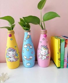 three colorful vases with plants in them sitting on a table next to some books