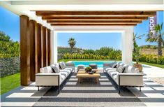 an outdoor living area with couches and tables next to a swimming pool in the background