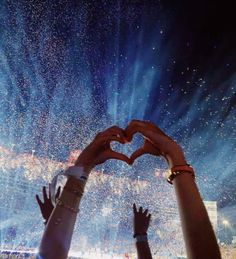 two hands making a heart shape in front of a crowd at a concert with bright lights