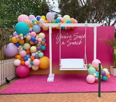 a pink backdrop with balloons and a swing