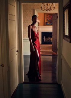 a woman in a red dress is standing at the door to her room and looking off into the distance