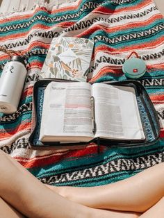 an open book sitting on top of a blanket next to a cup and some other items