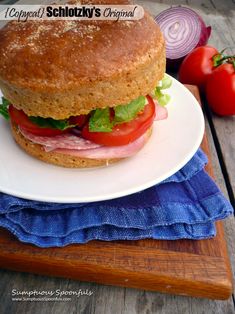 a large sandwich sitting on top of a white plate next to some tomatoes and onions