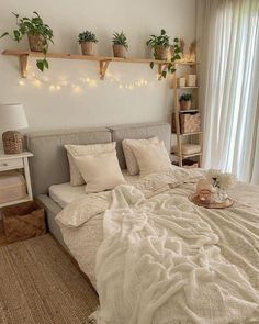 a bed with pillows, blankets and plants on the headboard is in front of a window