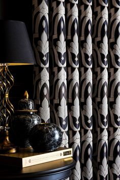 a lamp and vase on a table in front of curtained windows with black and white designs