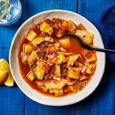 a white bowl filled with stew next to two lemons