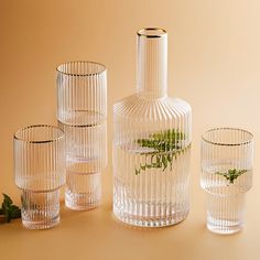 four clear glass vases with plants in them on a tan surface, one is empty and the other two are half full