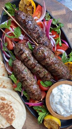 an assortment of meat skewers and vegetables on a plate with pita bread