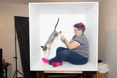 a woman sitting in front of a white box with a cat on it's back