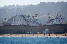 an amusement park with people on the beach and roller coasters in the background,