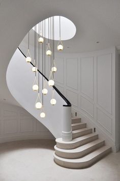 a spiral staircase with lights hanging from the ceiling and white walls in an empty room