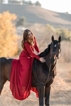 a woman in a red dress is riding a black horse and posing for the camera