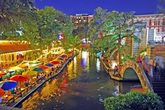 a river runs through the center of a city at night with umbrellas on it