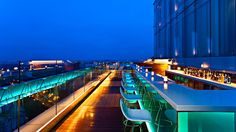 an outdoor bar overlooking the city lights at night with long tables and chairs lined up