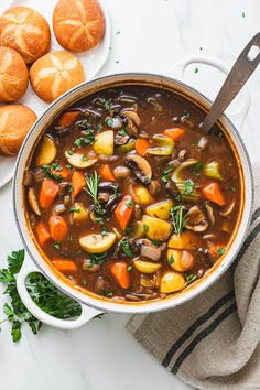 a pot filled with stew next to rolls