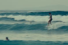 a woman riding a wave on top of a surfboard in the ocean next to another person