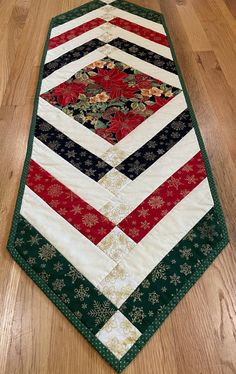 a quilted table runner on the floor with red, green and white flowers in it