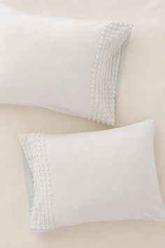 two white pillows sitting next to each other on top of a pillow case with scalloped edges