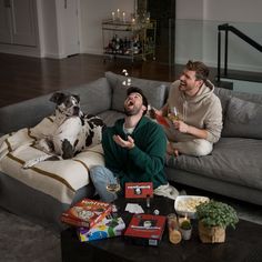 two men sitting on a couch with a dog