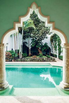 an outdoor swimming pool surrounded by columns and arches with a tree in the middle on one side