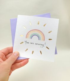 someone holding up a card that says you are amazing with a rainbow in the background