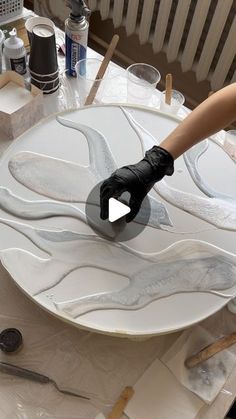 a person with gloves on painting a white plate