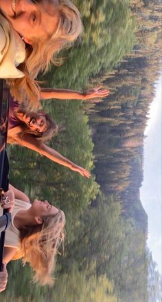 two women standing next to each other with trees in the background and water reflecting them